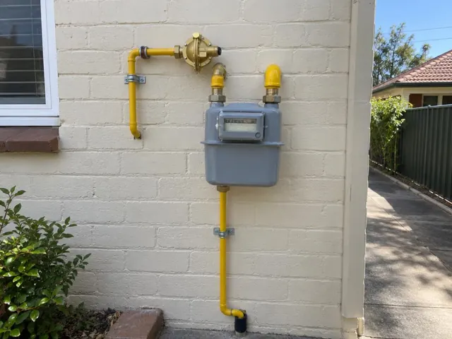 Gas meter and yellow gas pipes on a painted brick exterior wall beside a driveway in Hurstville