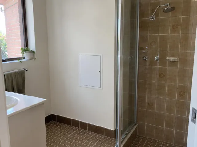Bathroom wall with small access panel beside a shower and tiled floor in Kingsgrove